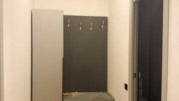 Ein schmaler Flur mit einer Tür rechts, einer Bank mit Handtuch und Schuh, sowie einer Wand-Klimaanlage.