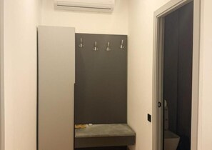 A narrow hallway with a door on the right, a bench with a towel and a shoe, and a wall-mounted air conditioning unit. - Imperial Hotel (Kapan)