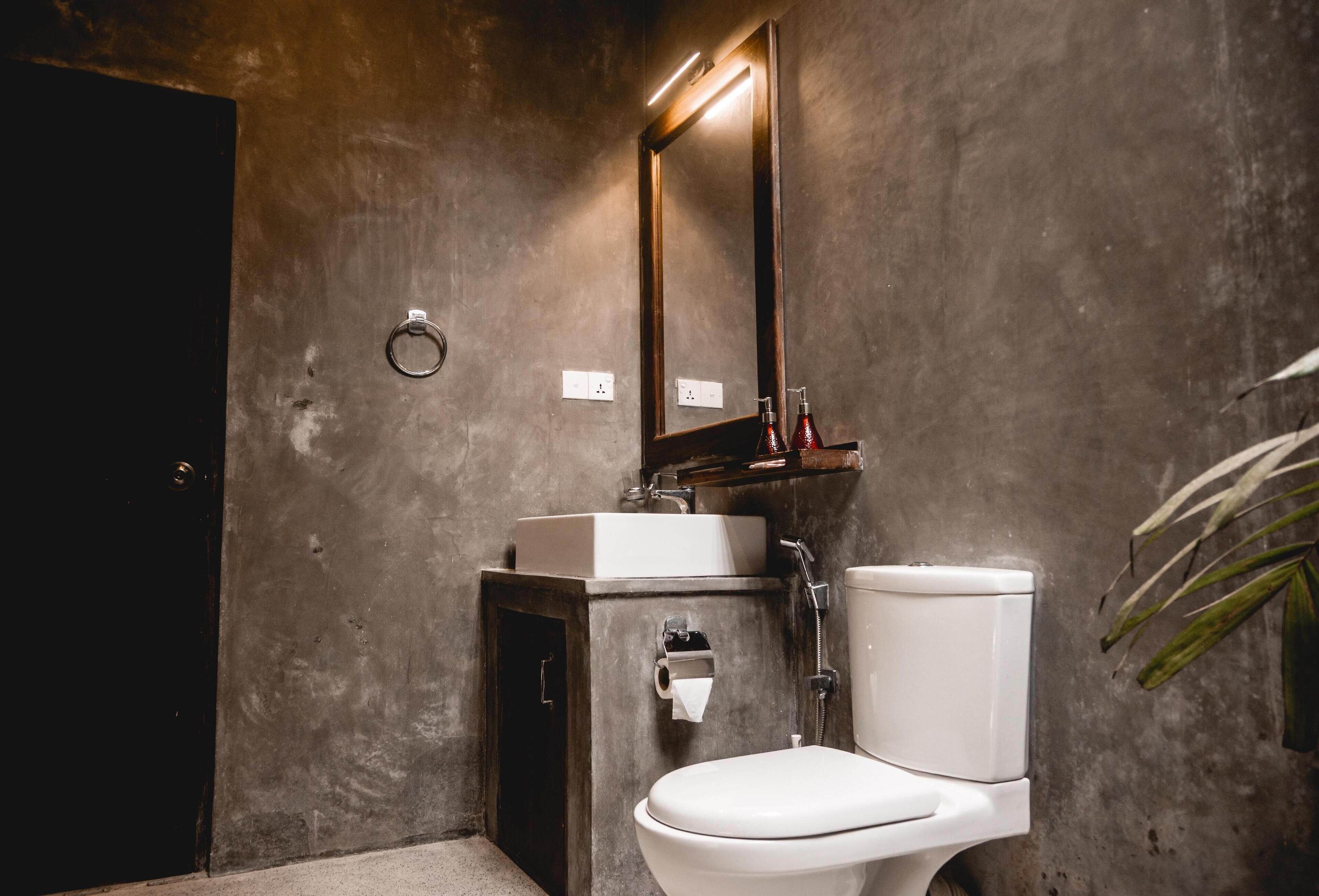 Une salle de bain moderne avec des toilettes blanches, un miroir rectangulaire et un petit lavabo.