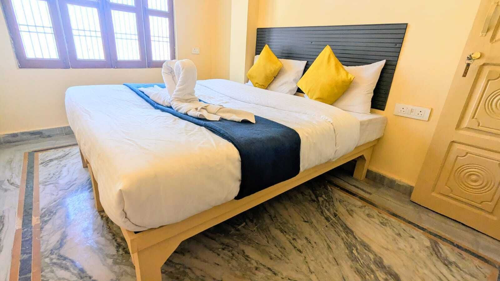 A bed with white linens, a blue blanket, and two yellow pillows.