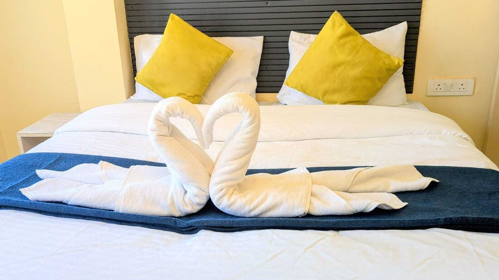 A neatly made bed with a blue bedspread and two white towels arranged in a swan shape.
