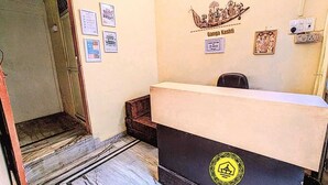 A reception area with a reception desk, a wall-mounted sign reading "Ganga Kashti," and several framed certificates or notices on the wall. - GANGA KASHTI (Varanasi)