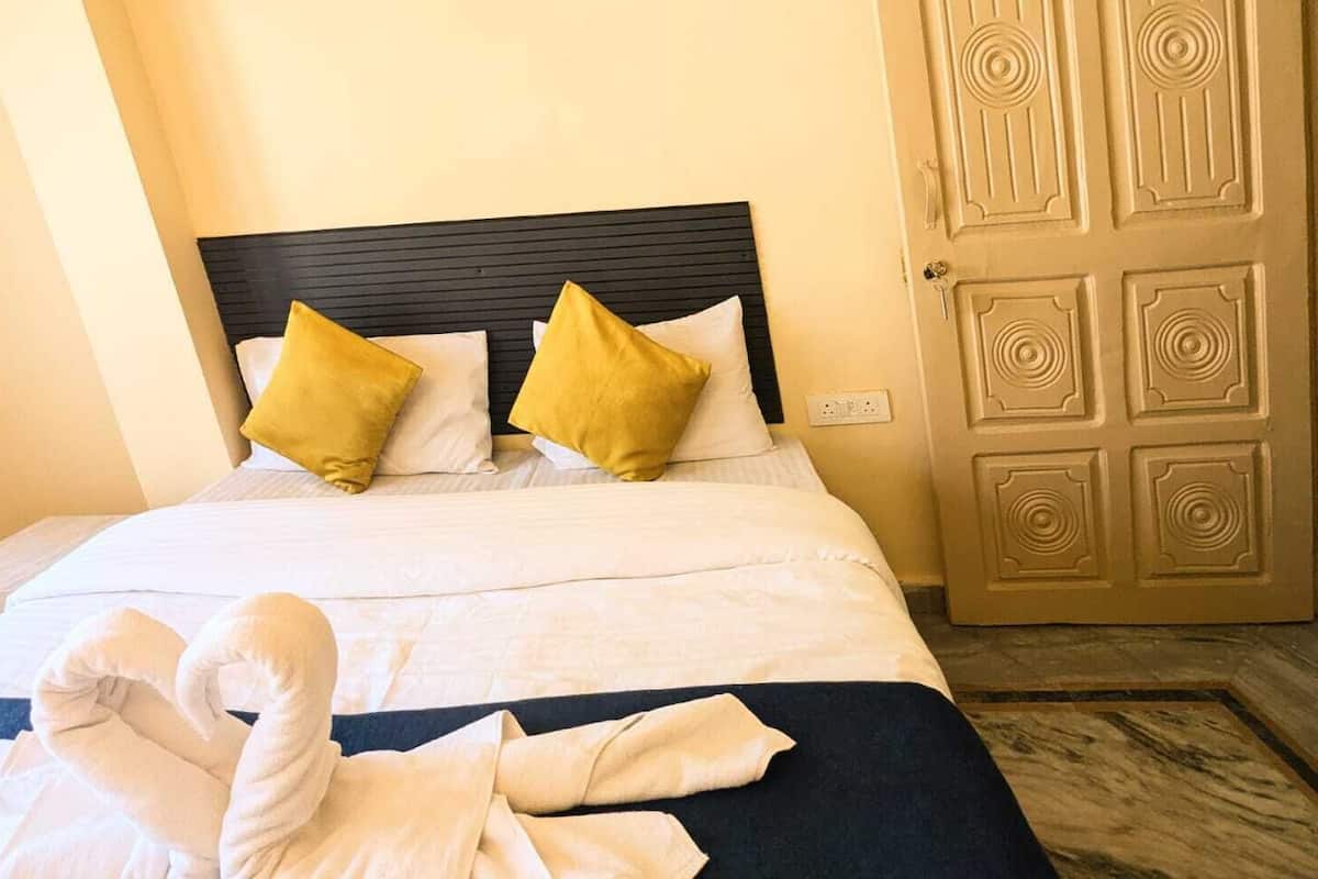 A neatly made bed with white linens and two yellow pillows, a dark headboard, and a wooden door with a geometric pattern.