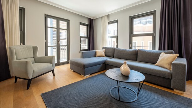 Un salon moderne avec un canapé d’angle gris, un fauteuil gris et une table basse ronde.