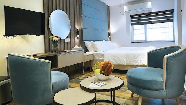 A hotel room with a bed, a TV, a desk, two chairs, a round table, and a bowl of fruit. - Sri Suryas Hotels (Colombo)