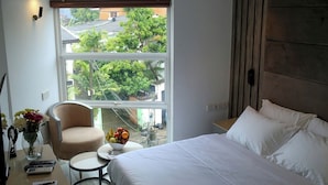 A hotel room with a large window, a bed, a chair, a small table with fruit, and a vase with flowers. - Sri Suryas Hotels (Colombo)