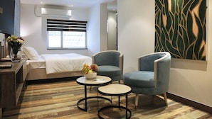 A modern hotel room with a bed, two armchairs, a small table with fruit, a TV, and a large abstract painting on the wall. - Sri Suryas Hotels (Colombo)