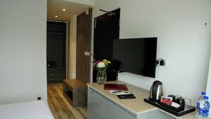 A hotel room with a bed, a small desk with a mirror, a TV, and a window. - Sri Suryas Hotels (Colombo)