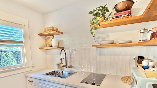 A modern kitchen with white cabinetry, a stainless steel sink, a built-in stove, and wooden shelves above the countertop. - Coastal Beach Bungalow walking distance to beach, coffee, and restaurants (Redondo Beach)