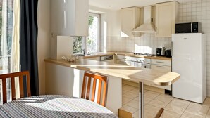 A modern kitchen with a dining area, featuring a kitchen island, white cabinets, and a built-in microwave. - Prime Location Apartment Châtelain Saint-gilles Quiet & Central (Brussels)