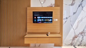 Quarto de hotel moderno com parede revestida em madeira, televisão montada exibindo a interface de um serviço de streaming e parede com padrão marmorizado.