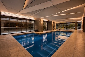 Ein Innenpool mit großen Glaswänden, Fliesenboden und einem modernen Deckenbau.
