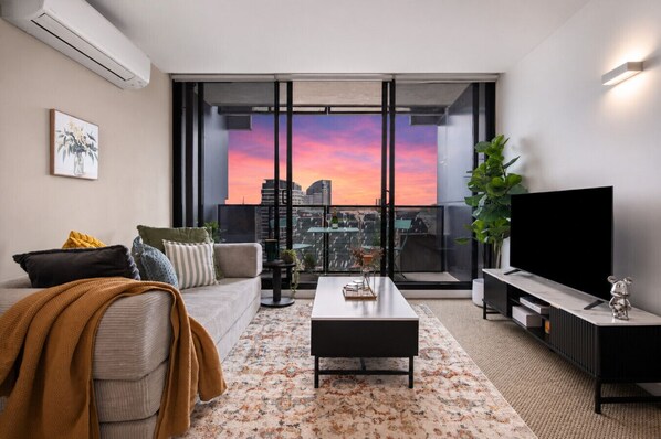 Ein modernes Wohnzimmer mit Sofa, Couchtisch, Fernseher und einem Balkon mit Blick auf die Stadt.