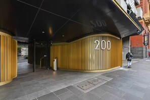 Ein moderner Gebäudeeingang mit einer geschwungenen Fassade, einem gut sichtbaren Schild mit der Aufschrift '200' und einem Metallmülleimer.