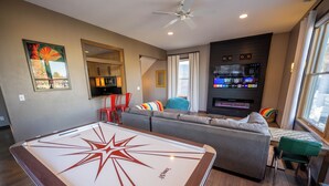 A modern living room with a pool table, a grey sofa, a TV wall unit, and a fireplace. - Family Retreat- Sauna, Arcade, Gym & Message Chair (Helena)