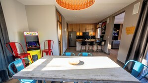 A modern kitchen with wooden cabinets, a stainless steel refrigerator, and a dining area with a wooden table and blue chairs. - Family Retreat- Sauna, Arcade, Gym & Message Chair (Helena)