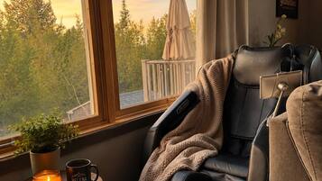 Un fauteuil de massage de la marque BOSSCARE, placé dans une pièce dotée d’une grande fenêtre, d’une plante en pot, d’une bougie et d’une tasse.