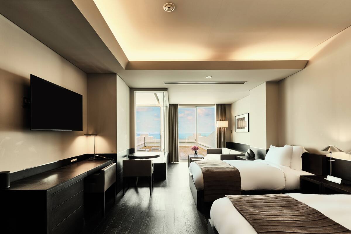 A hotel room with a bed, a desk, a chair, a TV, and a view of the outdoors.
