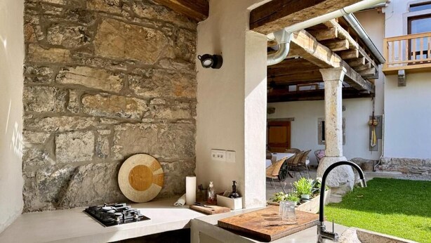 Un mur de pierre, une planche à découper en bois, un évier et un petit jardin visible à travers une porte ouverte.