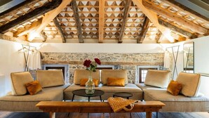 Un salon chaleureux, aménagé dans un style industriel, avec une cheminée en pierre, des poutres en bois et un grand canapé agrémenté de coussins.