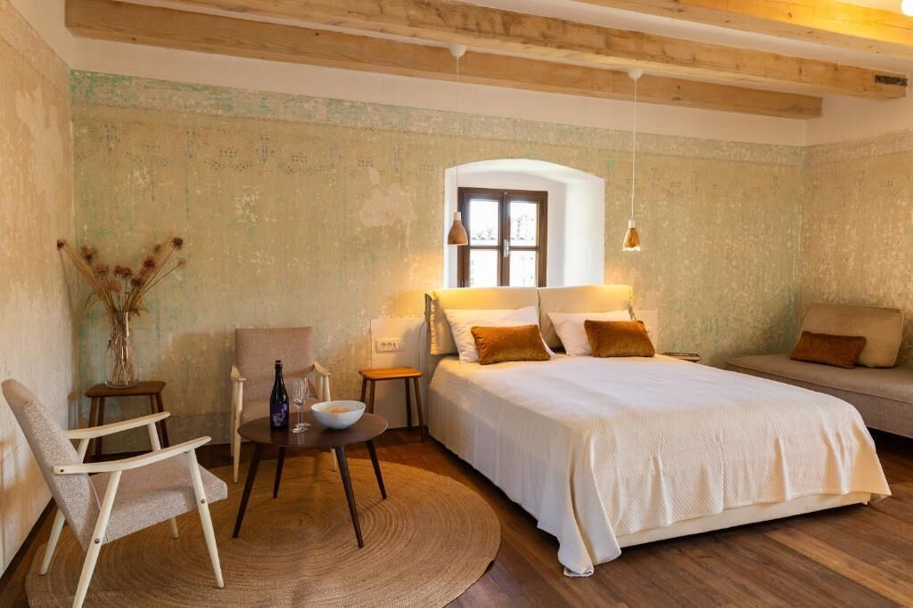 Un dormitorio con cama, una silla, una mesita y un ventanal.