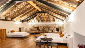 Une pièce chaleureuse et rustique avec un plafond en pente, des poutres apparentes, une cheminée et un lit à baldaquin blanc.