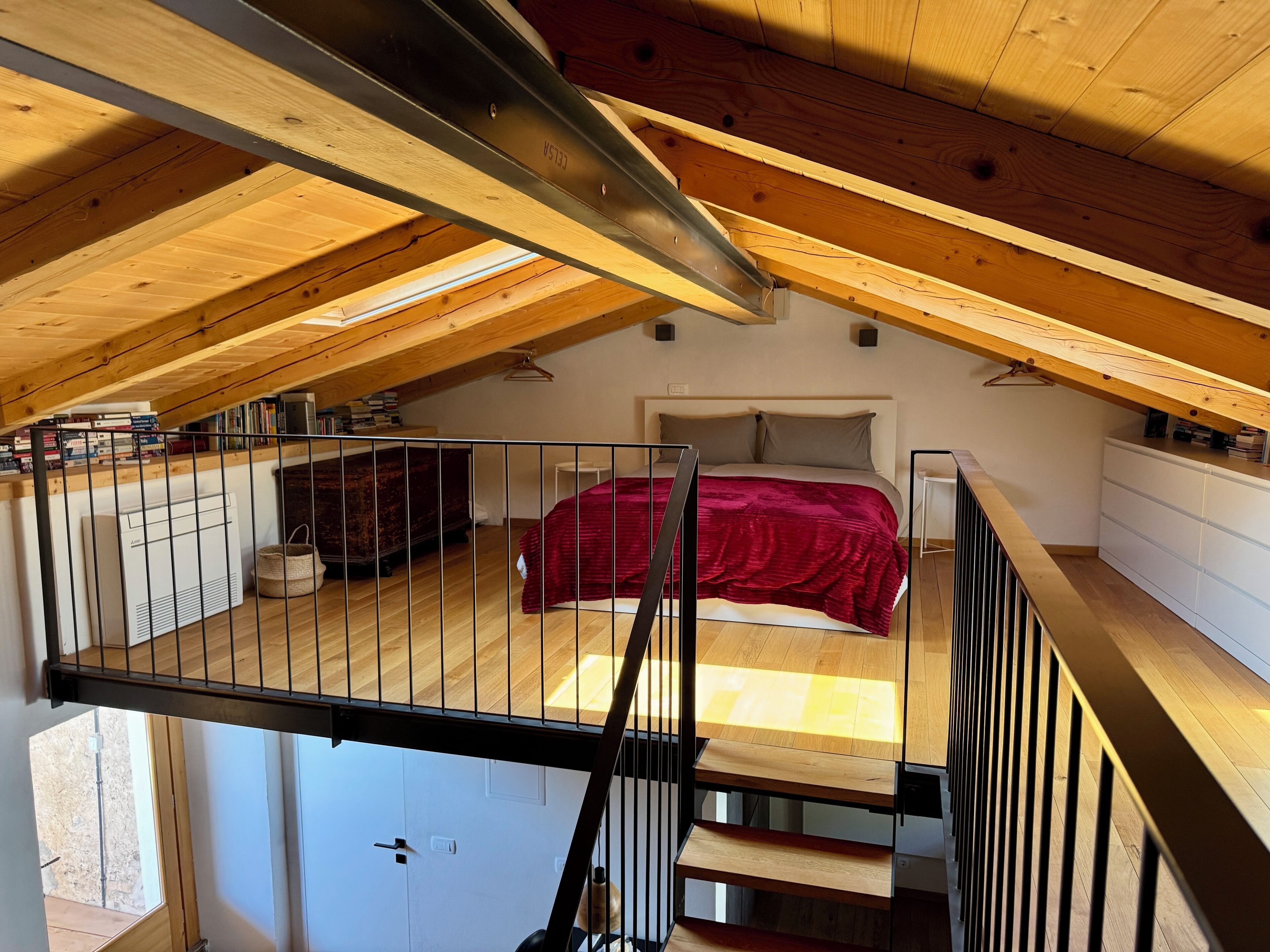 Een slaapkamer met een schuine kap, een bed met een rode deken en een witte dressoir.