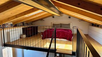 Een slaapkamer met een schuine kap, een bed met een rode deken en een witte dressoir.