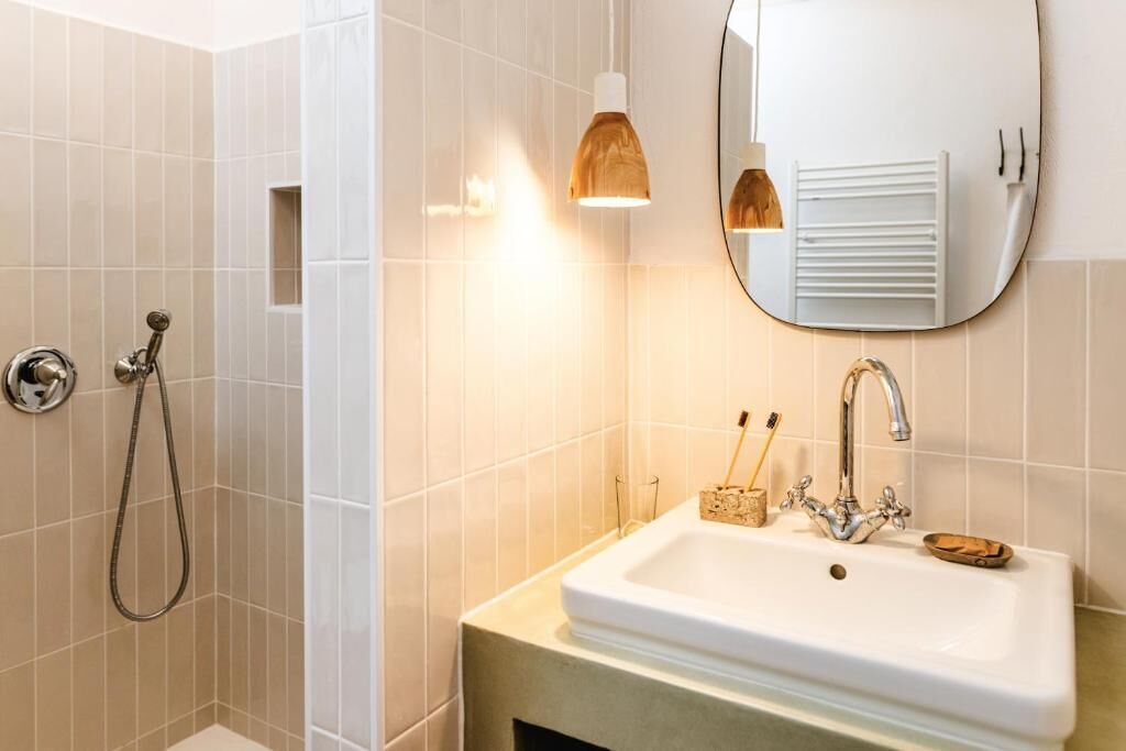 A bathroom with a white sink, a mirror, a handheld showerhead, and a towel rack.