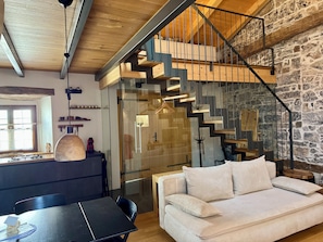 Un interior modern amb sostre de fusta, paret de pedra, una escala i un sofà.