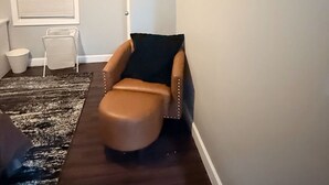En moderne stue med en lædersofa i brunt, et stort abstrakt maleri, en hvid stol og et mørkebrunt tæppe.