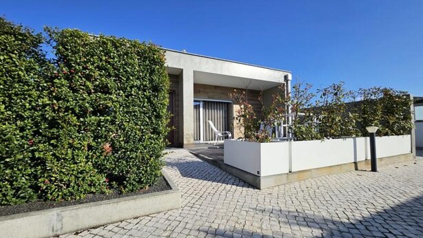 A modern building with a paved courtyard, a white exterior, and a well-maintained hedge. - Rainbow Apartments in Marinha Grande (Marinha Grande)