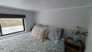 Quarto com cama, janela e mesa de cabeceira com um vaso.