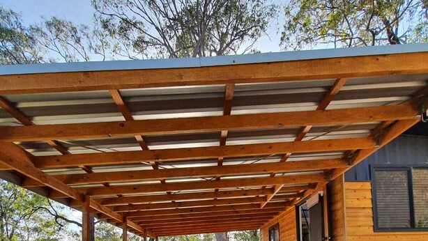 Um deck de madeira com pérgola, rodeado por plantas e árvores.