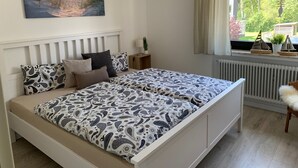 A bedroom with a bed, a nightstand, a window with a view of greenery, and a painting on the wall. - Apartment "Halvar" with Balcony and WiFi (Maasholm)