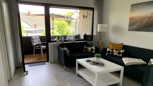 A modern living room with a black sofa, white coffee table, and a view through a glass door to the outside. - Apartment "Halvar" with Balcony and WiFi (Maasholm)