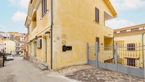 A yellow building with a stone-paved entrance, a metal gate, and a visible number '78' on the wall. - With beachfront terrace and air conditioning (Castelsardo)