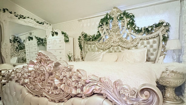 Ein luxuriöses Schlafzimmer mit einem gepolsterten Kopfteil, aufwendigen Blumendekorationen und einem Spiegel mit verziertem Rahmen.