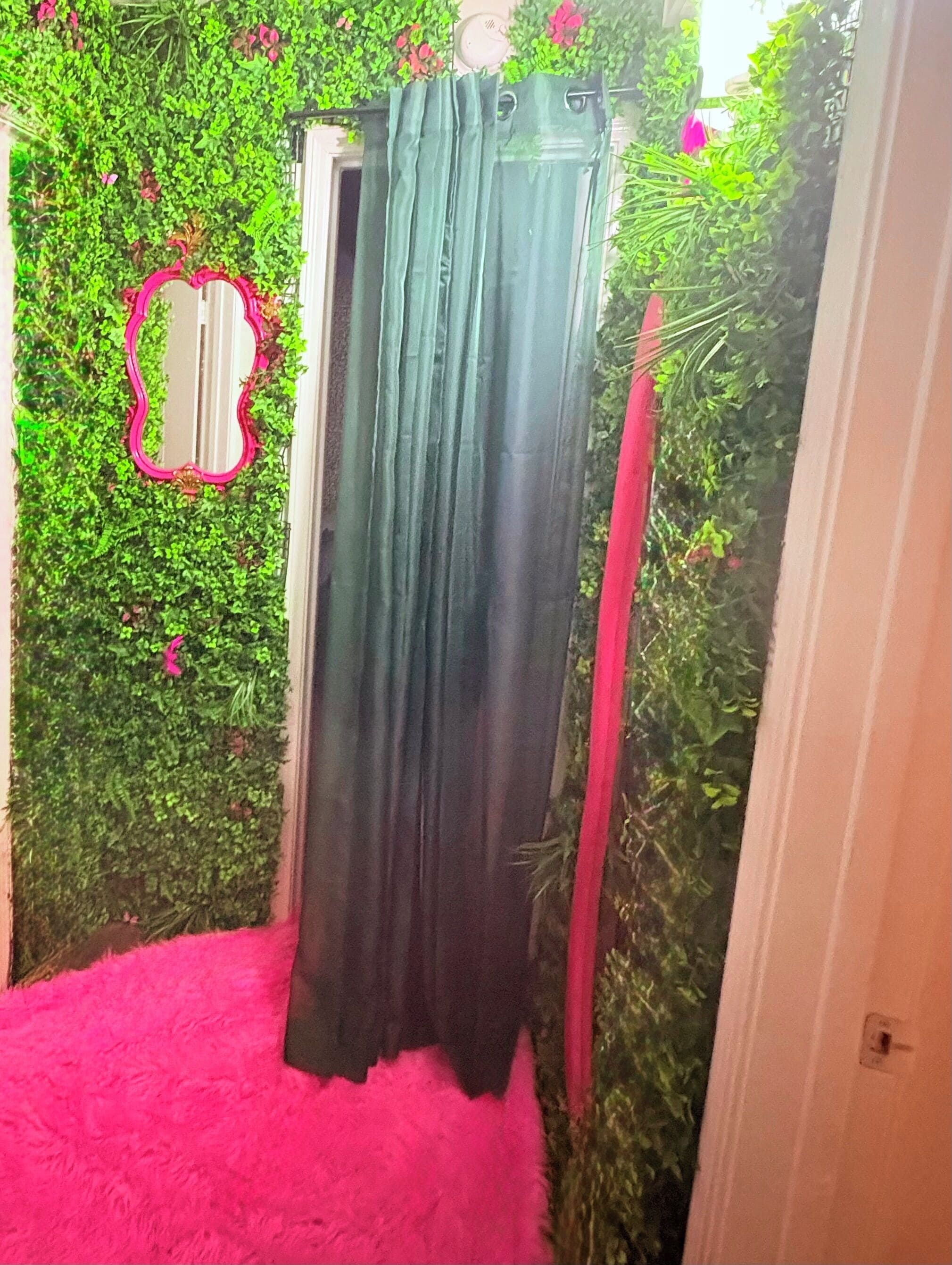 A room with a green curtain, a pink fluffy rug, and a heart-shaped mirror.