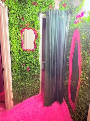 Ein Zimmer mit grüner Wand, einem Spiegel, einem Vorhang und einem flauschigen rosa Teppich.