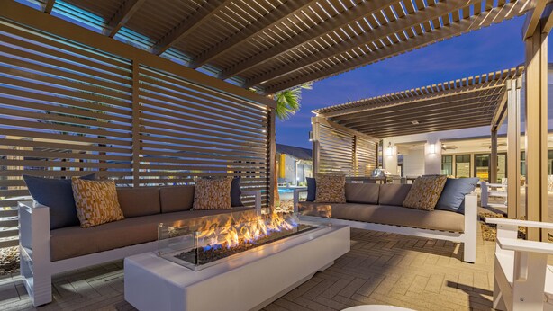 An outdoor seating area with a fire feature, white furniture, and a covered pergola. - Sleeps 20 | Two 4BR Homes | Resort Pool + Hot Tub + Firepit | Summerwell (Thermal)