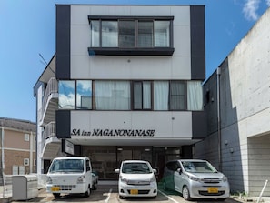 Un edificio de varios pisos con un cartel que dice 'SA inn NAGANONANASE'. Hay tres coches estacionados en la parte delantera.
