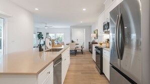 Et moderne køkken med en stor ø, rustfrie hvidevarer og et spiseområde med et bord og stole.