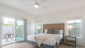 Et soveværelse med seng, ventilator, natbord og udsigt gennem en skydedør.