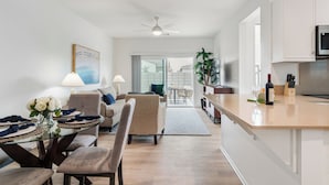 Et moderne køkken med hvide skabe, en mikrobølgeovn og et spiseområde med et glasbord og stole.