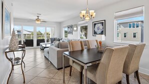 A spacious living area with a dining table, sofa, and chairs, large windows, and a ceiling fan. - Exclusive Beach Access + Private Pool + Sunset Views | Sandy Pelican (Seacrest)