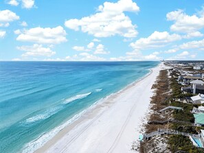 A coastal view with a beach, ocean, and beachfront properties. - Exclusive Beach Access + Private Pool + Sunset Views | Sandy Pelican (Seacrest)