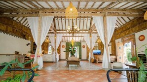 A spacious room with a high ceiling, wooden beams, a chandelier, and a central seating area with a table and chairs. - Sacred Jewel by GenuineHost (Payangan)