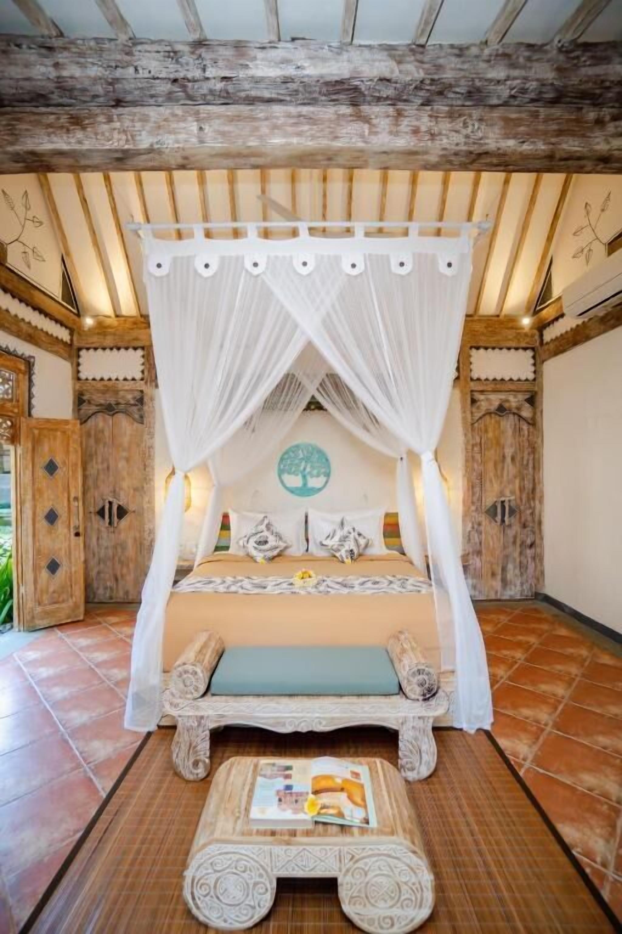 Une chambre avec un lit à baldaquin, une petite table sur laquelle est posé un magazine et un élément décoratif mural.