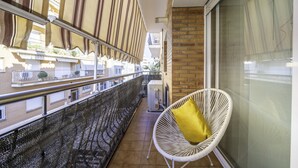 A balcony with a white chair and a yellow cushion, a metal railing, and a view of a building with balconies. - HomeHolidaysRentals Coquette - Costa Barcelona (Pineda de Mar)